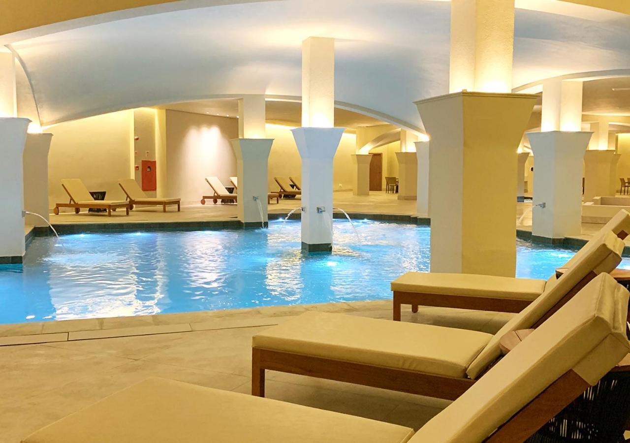 Buona Vitta Gramado Resort & Spa By Gramado Parks Exterior photo The photo shows an indoor spa or relaxation area with a tranquil atmosphere. There is a large swimming pool with clear blue water, illuminated by soft lighting. Surrounding the pool are several comfortable lounge chairs. The architecture features ele