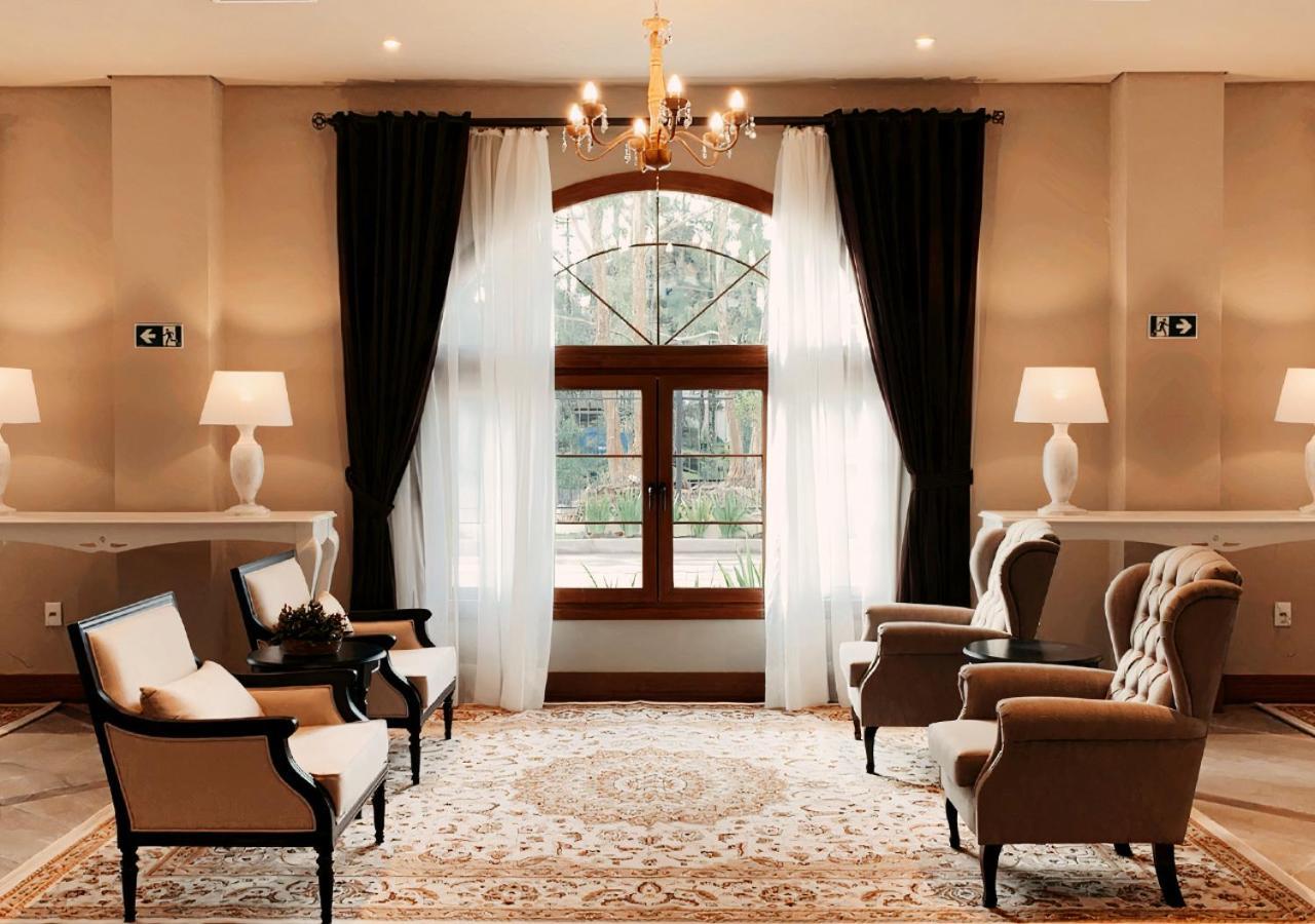 Buona Vitta Gramado Resort & Spa By Gramado Parks Exterior photo The photo shows an elegantly styled living room. There are two armchairs and a sofa arranged comfortably around an intricate area rug. Large windows are adorned with sheer white curtains and dark curtains, allowing natural light to fill the space. A 