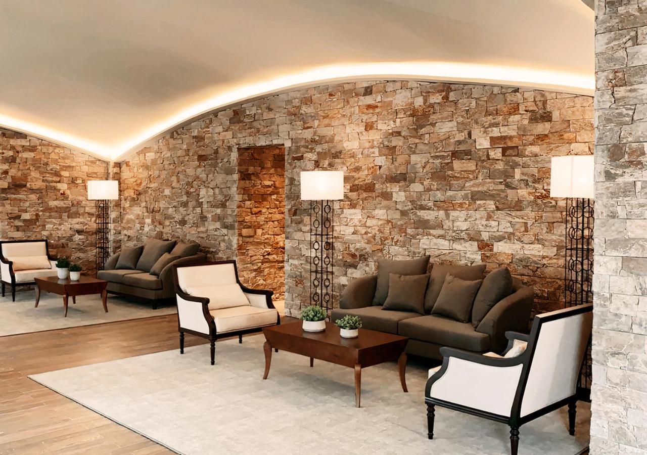 Buona Vitta Gramado Resort & Spa By Gramado Parks Exterior photo The photo shows a stylish and modern lounge area. The walls are made of natural stone, creating a warm and inviting atmosphere. There are two comfortable sofas in a muted gray color arranged around a wooden coffee table. Flanking the sofas are elegan