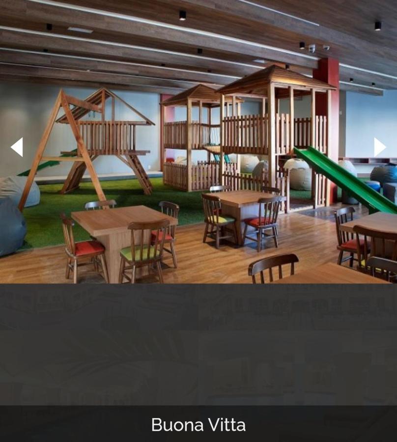 Buona Vitta Gramado Resort & Spa By Gramado Parks Exterior photo The photo shows a play area designed for children, featuring a wooden play structure with slides and climbing areas. In the foreground, there are several small wooden tables and chairs arranged for seating. The floor is covered with green turf, resem