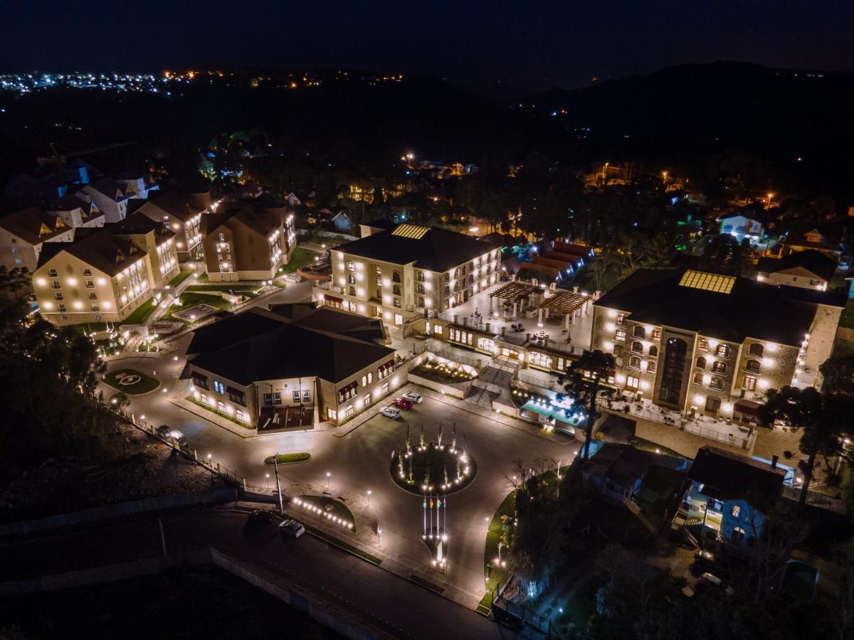 Buona Vitta Gramado Resort & Spa By Gramado Parks Exterior photo The photo shows a beautifully lit resort or hotel complex taken at night. The buildings are well-illuminated, highlighting their architecture. There is a circular area with a fountain at the center, surrounded by pathways that connect various parts o