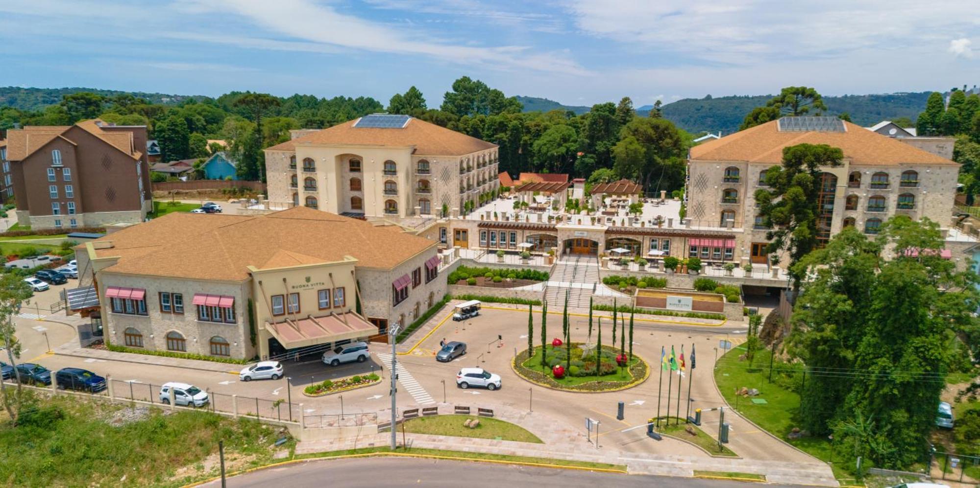 Buona Vitta Gramado Resort & Spa By Gramado Parks Exterior photo The photo shows an aerial view of a hotel complex surrounded by lush greenery. The buildings are designed with beige and light-colored facades, featuring multiple stories and a spacious layout. In the foreground, there is a circular road with several