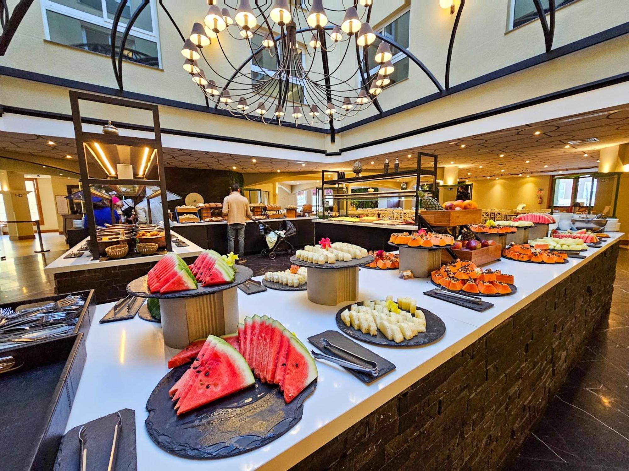 Buona Vitta Gramado Resort & Spa By Gramado Parks Exterior photo The photo depicts a lavish buffet setup in a dining area. In the foreground, there are several platters featuring an assortment of colorful food items, primarily fruits like watermelon and various types of sushi or rolls. The buffet table is elegantl