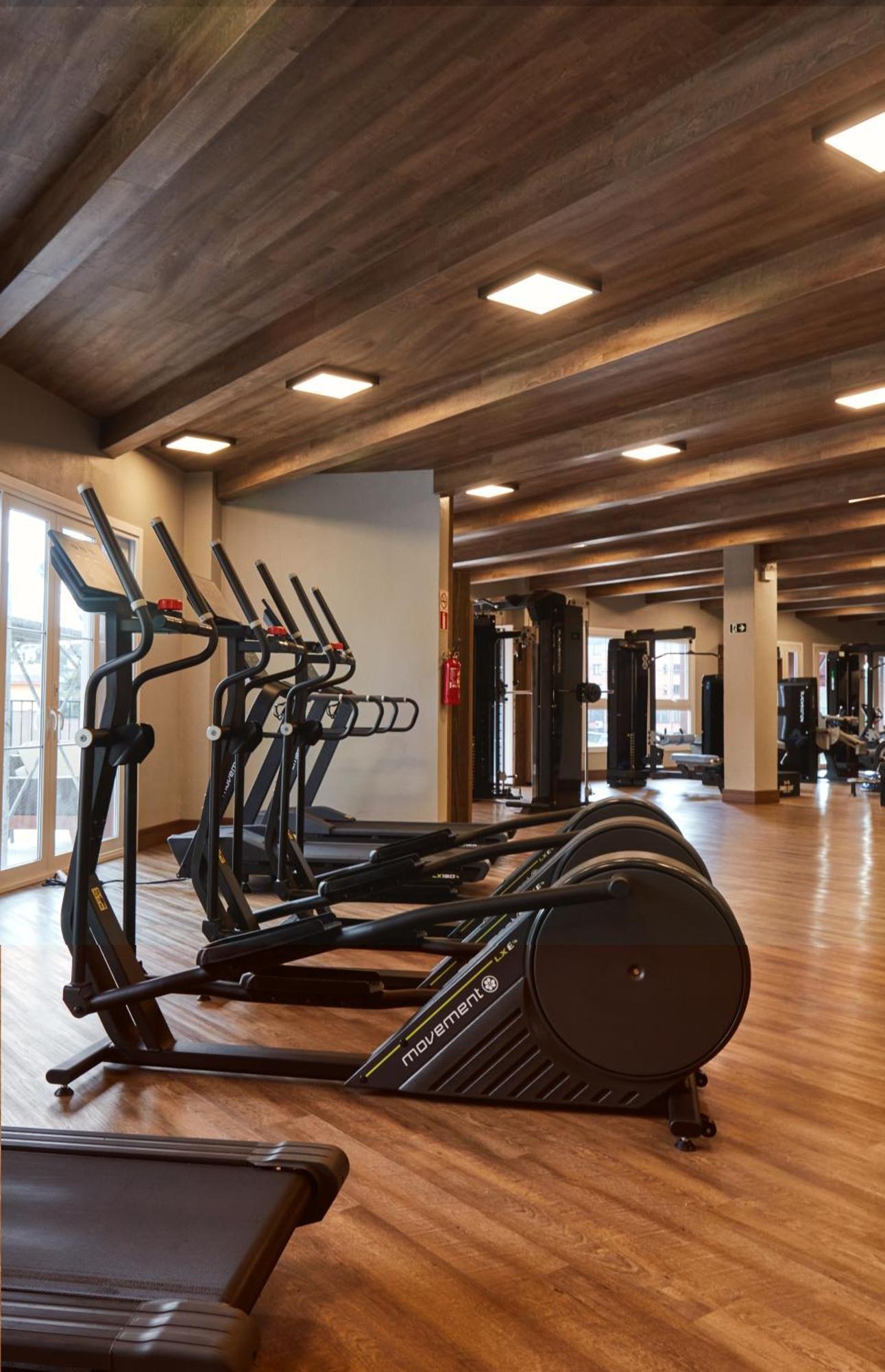 Buona Vitta Gramado Resort & Spa By Gramado Parks Exterior photo The photo shows a modern gym interior with wooden flooring and a ceiling with wooden beams. There are several exercise machines, including elliptical trainers and a treadmill, positioned in the foreground. In the background, there are additional work