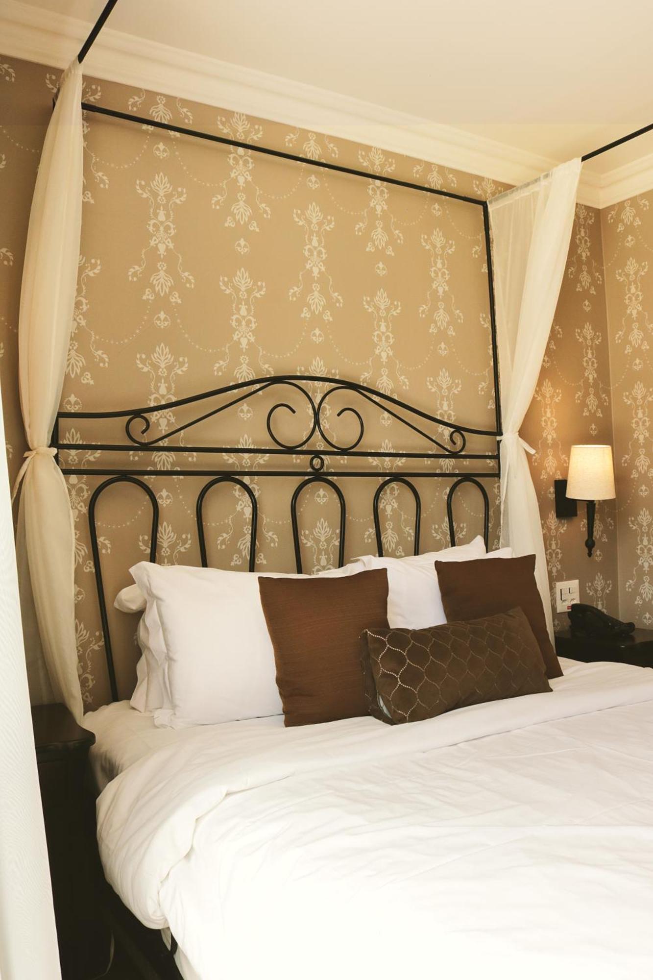 Buona Vitta Gramado Resort & Spa By Gramado Parks Exterior photo The photo shows a cozy bedroom setup featuring a decorative metal bed frame with a scroll design as the headboard. The bed is adorned with several white pillows and two brown decorative cushions. The wall behind the bed is covered with a light-colore
