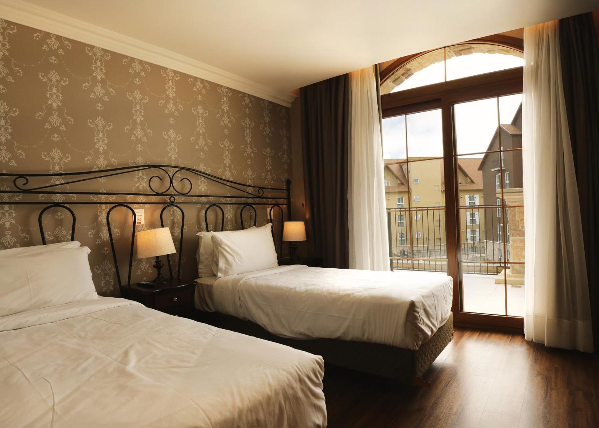 Buona Vitta Gramado Resort & Spa By Gramado Parks Exterior photo The photo shows a well-decorated hotel room featuring two beds. One bed is larger, likely a double bed, while the other is a single bed. The walls are adorned with a floral pattern, and there are bedside lamps next to the larger bed. Large windows wi