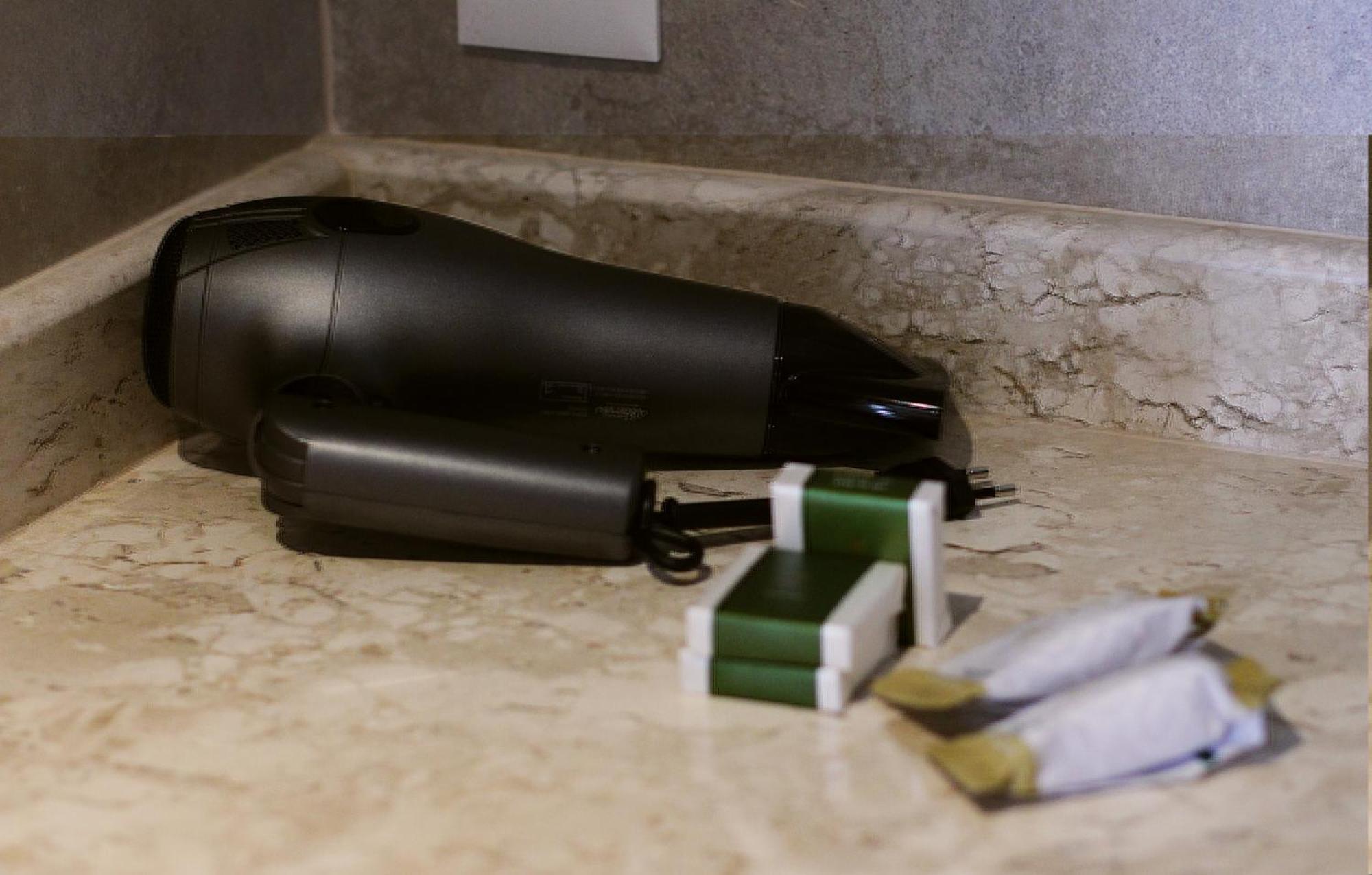 Buona Vitta Gramado Resort & Spa By Gramado Parks Exterior photo The photo shows a black hairdryer placed on a marble countertop. Next to the hairdryer, there are two wrapped items, likely toiletries, with green and white packaging. Additionally, there are two more items, also wrapped, which appear to be in simila