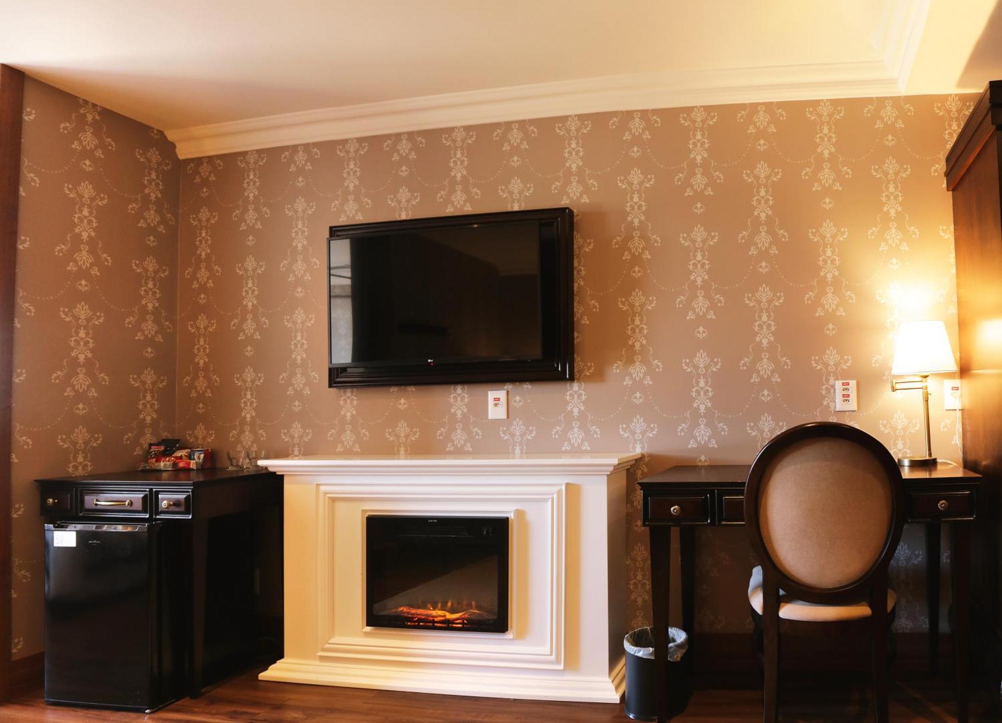 Buona Vitta Gramado Resort & Spa By Gramado Parks Exterior photo The photo shows a cozy room featuring a decorative wall with a subtle pattern. On one side, there is a modern flat-screen television mounted on the wall. Below it, there is a stylish electric fireplace framed in white. Adjacent to the fireplace is a 