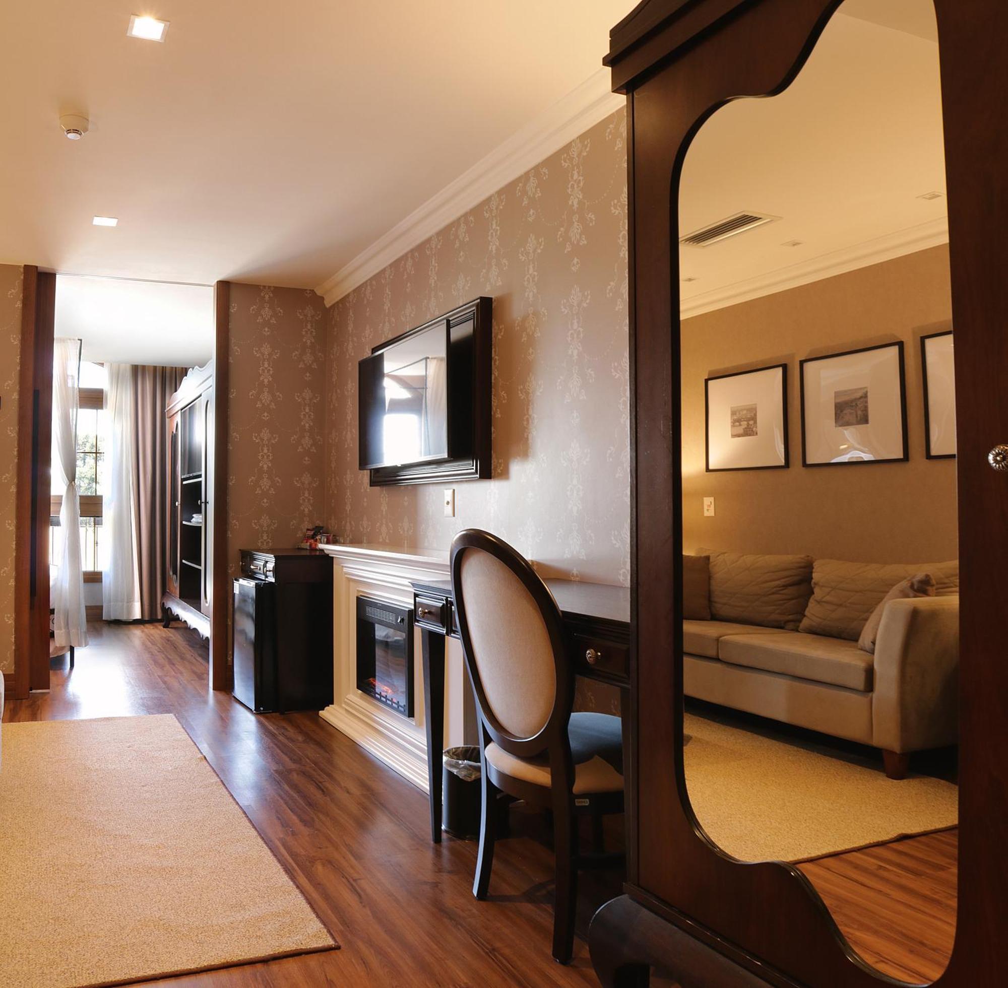 Buona Vitta Gramado Resort & Spa By Gramado Parks Exterior photo The photo shows a well-decorated room that appears to be a living area or a hotel suite. In the foreground, there is a round chair and a desk. A large mirror reflects the living space, creating a sense of spaciousness. 

On the wall is a flat-screen 