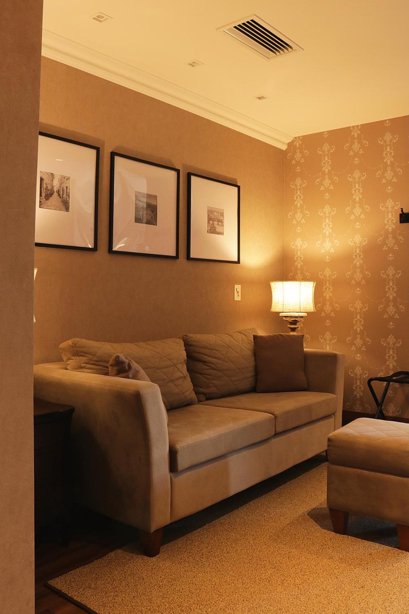 Buona Vitta Gramado Resort & Spa By Gramado Parks Exterior photo The photo shows a cozy living room setting. There is a light-colored sofa adorned with several cushions, positioned against a wall that has a subtle pattern. Above the sofa, there are three framed artworks or photographs hanging on the wall. To the s