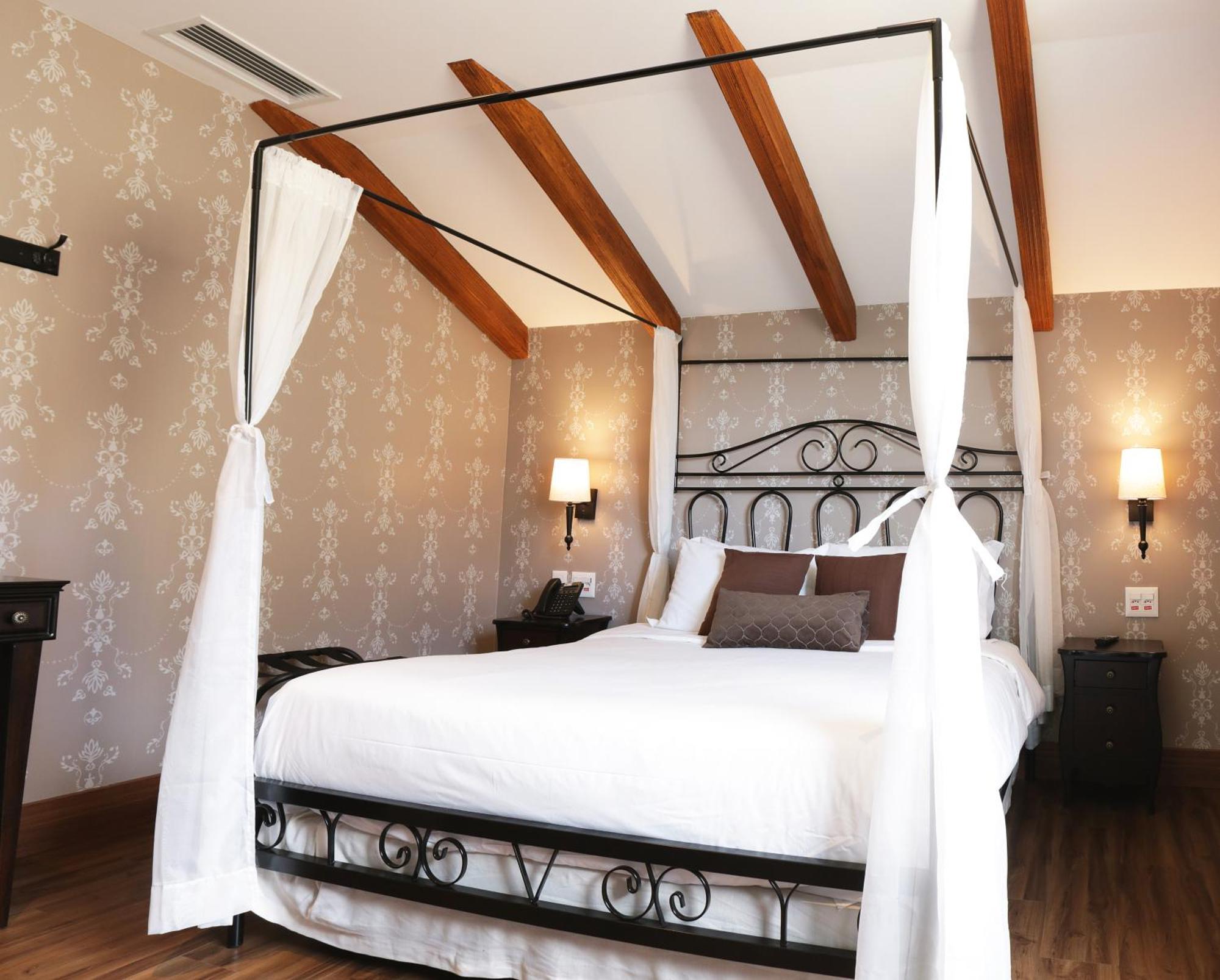 Buona Vitta Gramado Resort & Spa By Gramado Parks Exterior photo The photo shows a beautifully designed bedroom featuring a four-poster bed with a metal frame and flowing white curtains. The bed is adorned with white bedding and brown decorative pillows. The room has wooden beams on the ceiling and is decorated wi