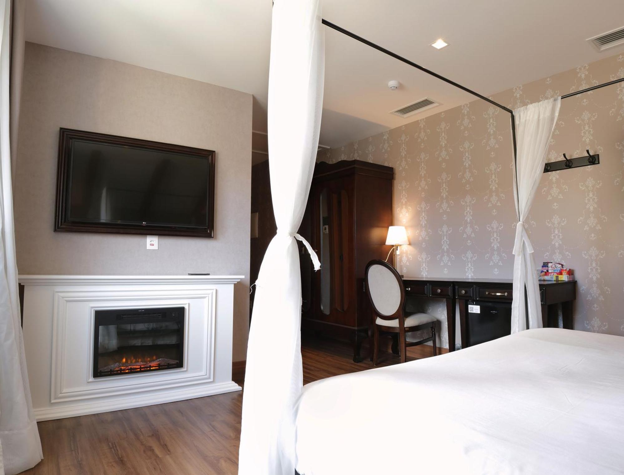 Buona Vitta Gramado Resort & Spa By Gramado Parks Exterior photo The photo shows a cozy hotel room with elegant decor. There is a white bed with a canopy, and a modern television mounted on the wall across from it. To the side, a fireplace is built into a white mantel, adding a warm touch to the space. There's a w