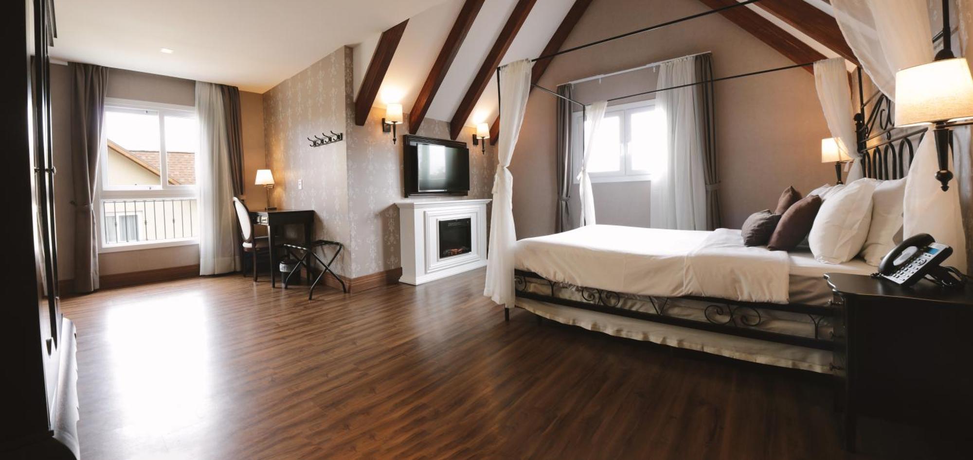Buona Vitta Gramado Resort & Spa By Gramado Parks Exterior photo The photo shows a spacious hotel room with a modern and elegant design. There is a large bed with an overhead canopy, and the bed is dressed in white linens. To the side, there is a small seating area with a desk and chair. A flat-screen television i